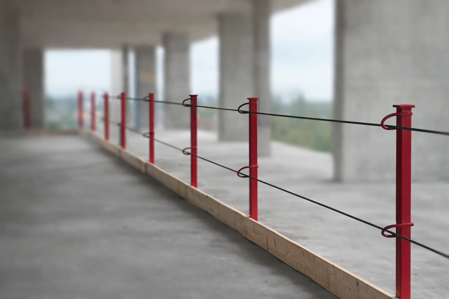 Installed perimeter guardrail with red stanchions and tensioned cable along a concrete slab edge